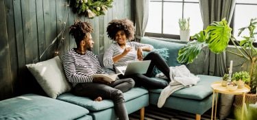 Man and woman talking about something on the couch with a laptop open.