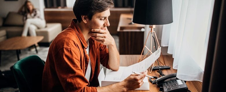 A man sits at a desk reading a piece of paper.