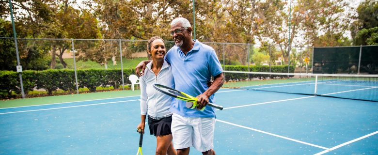 A couple walks arm in arm on a tennis court.