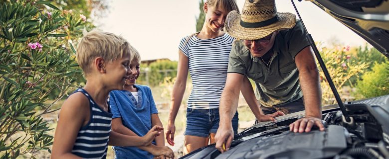 A man works on his car as his children look on.