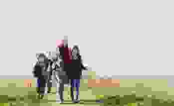 A young girl and boy walking with their grandma on the beach.