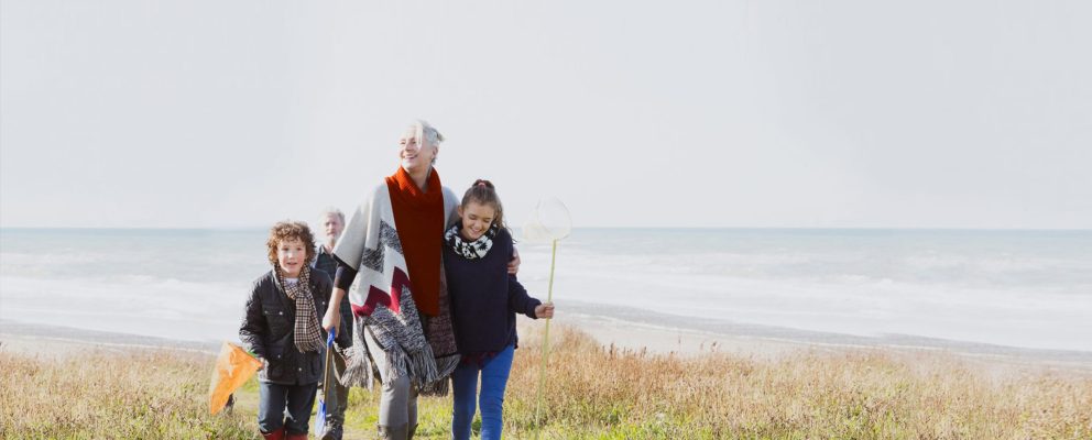 A young girl and boy walking with their grandma on the beach.