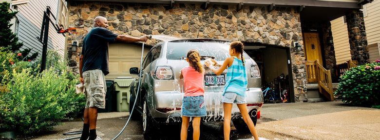 A man and his two young daughters wash their car in the driveway.