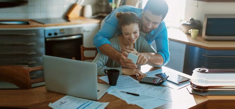 Couple looking at a mobile phone while reviewing paperwork in their kitchen