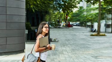 Woman carrying her laptop looks both ways before crossing the street.