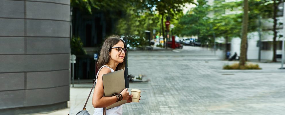 Woman carrying her laptop looks both ways before crossing the street.
