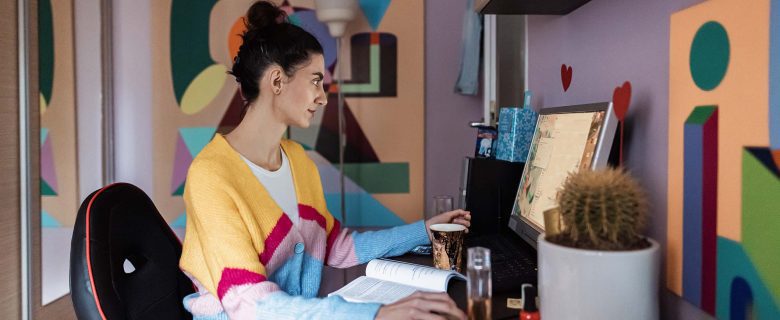 A woman sits in front of a desktop computer with a book on her desk.