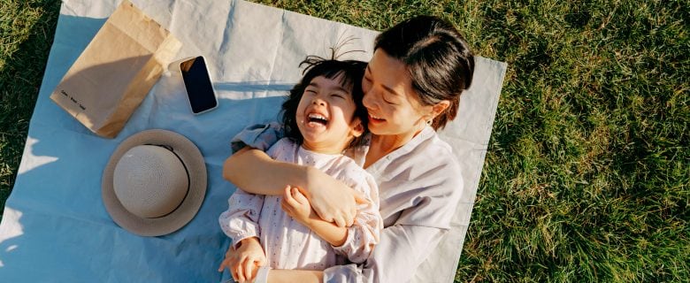 A woman holds her child on a blanket in the grass.