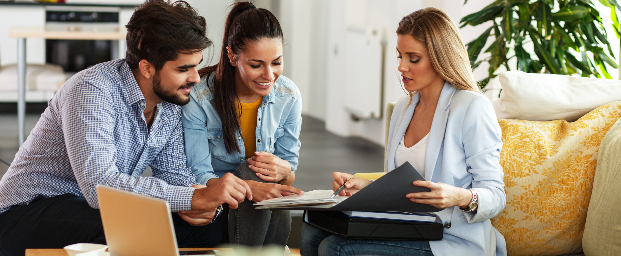 A man and woman look on as another women goes over documents in a folder.