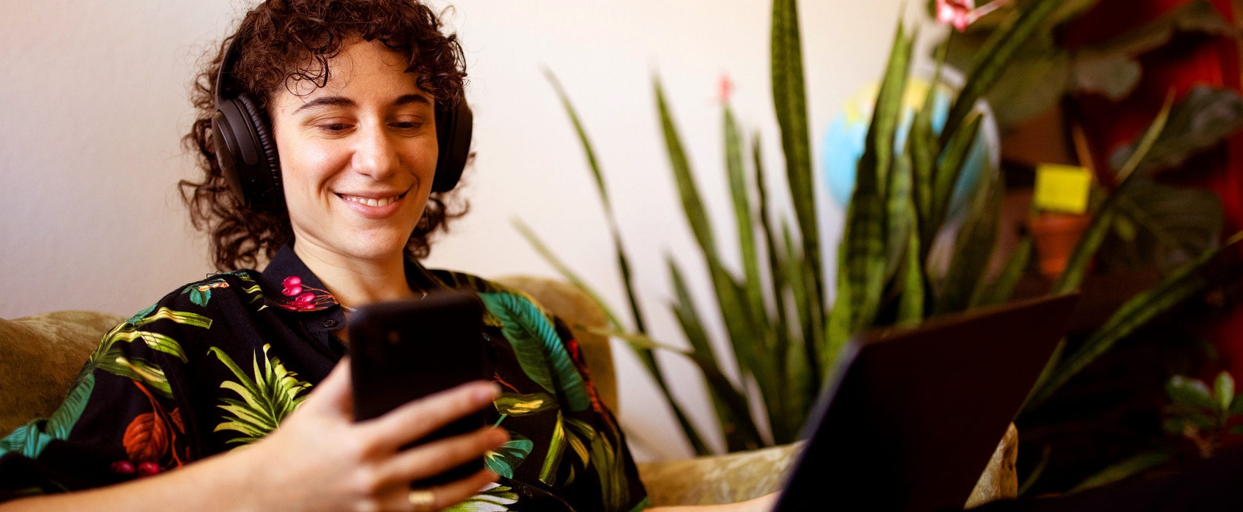 A person sitting on a sofa with headphones on, while looking at their mobile phone.