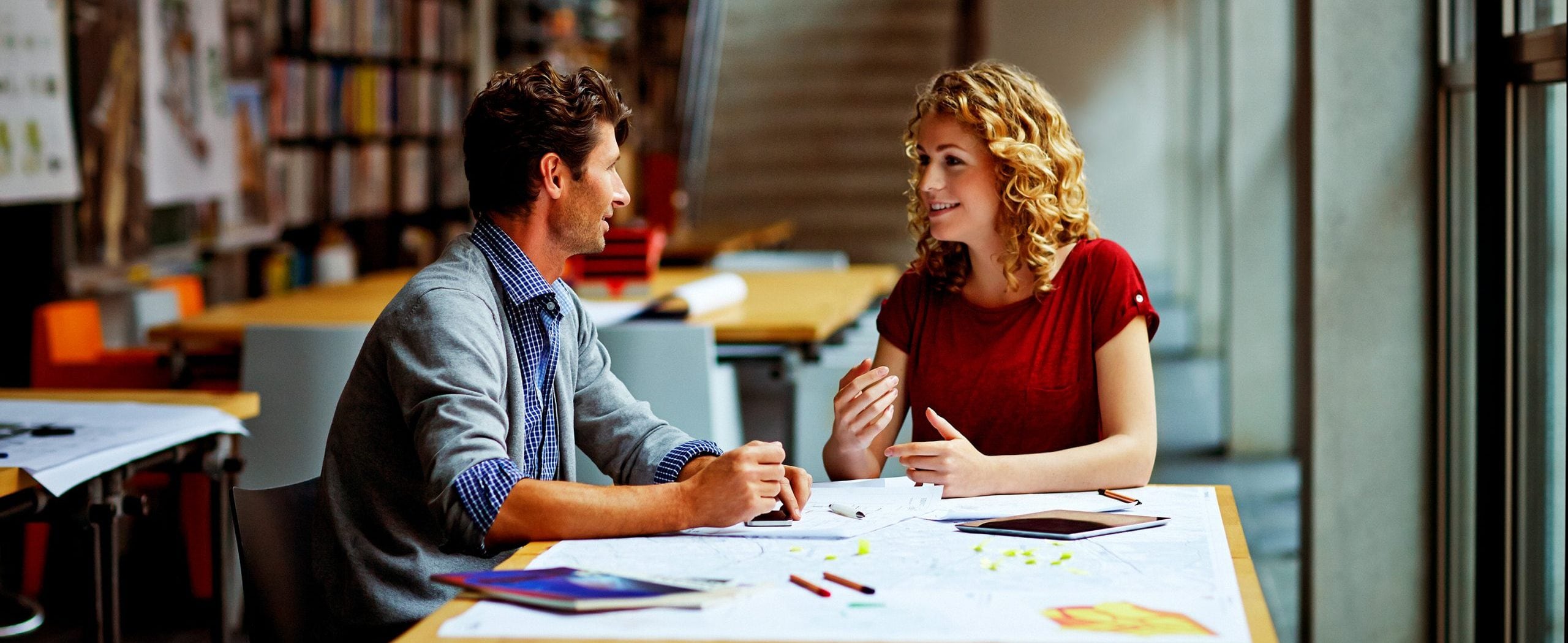 A man and a woman sit at a table talking.