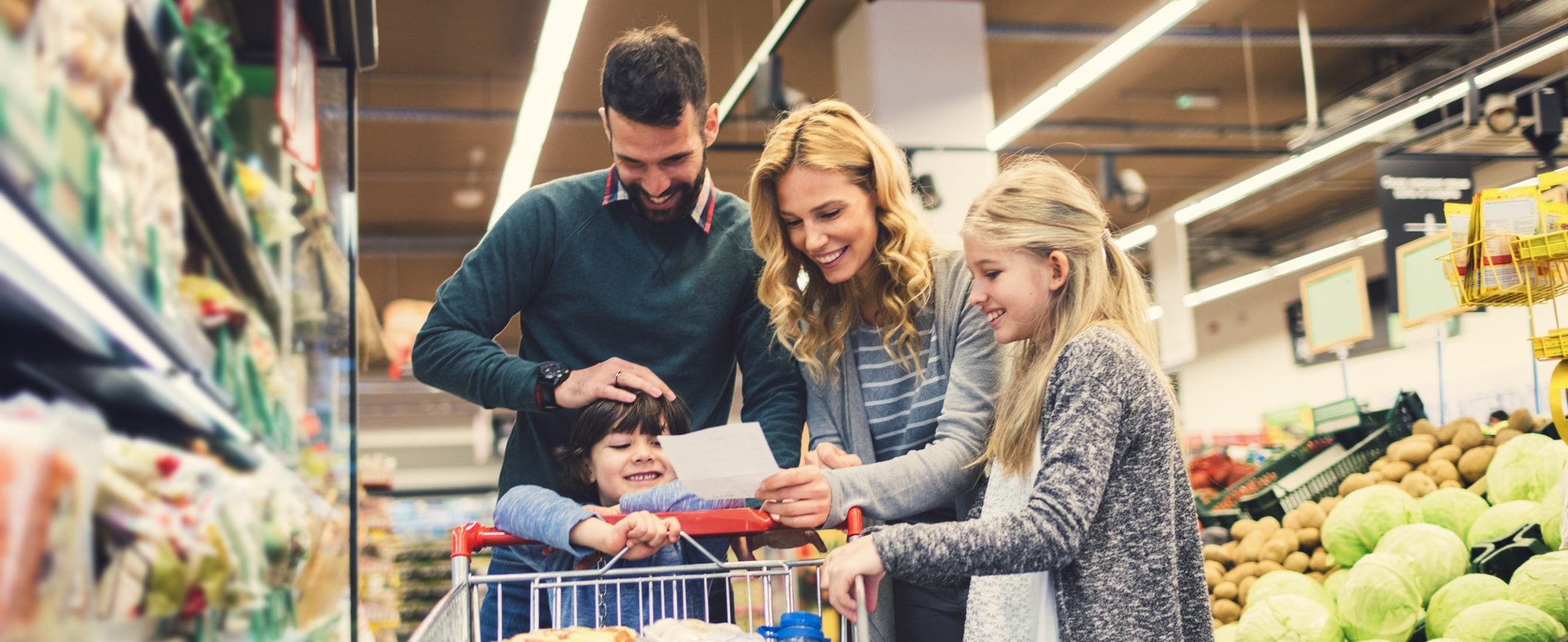 A family looking at a grocery list while huddled around a shopping cart in a grocery store.