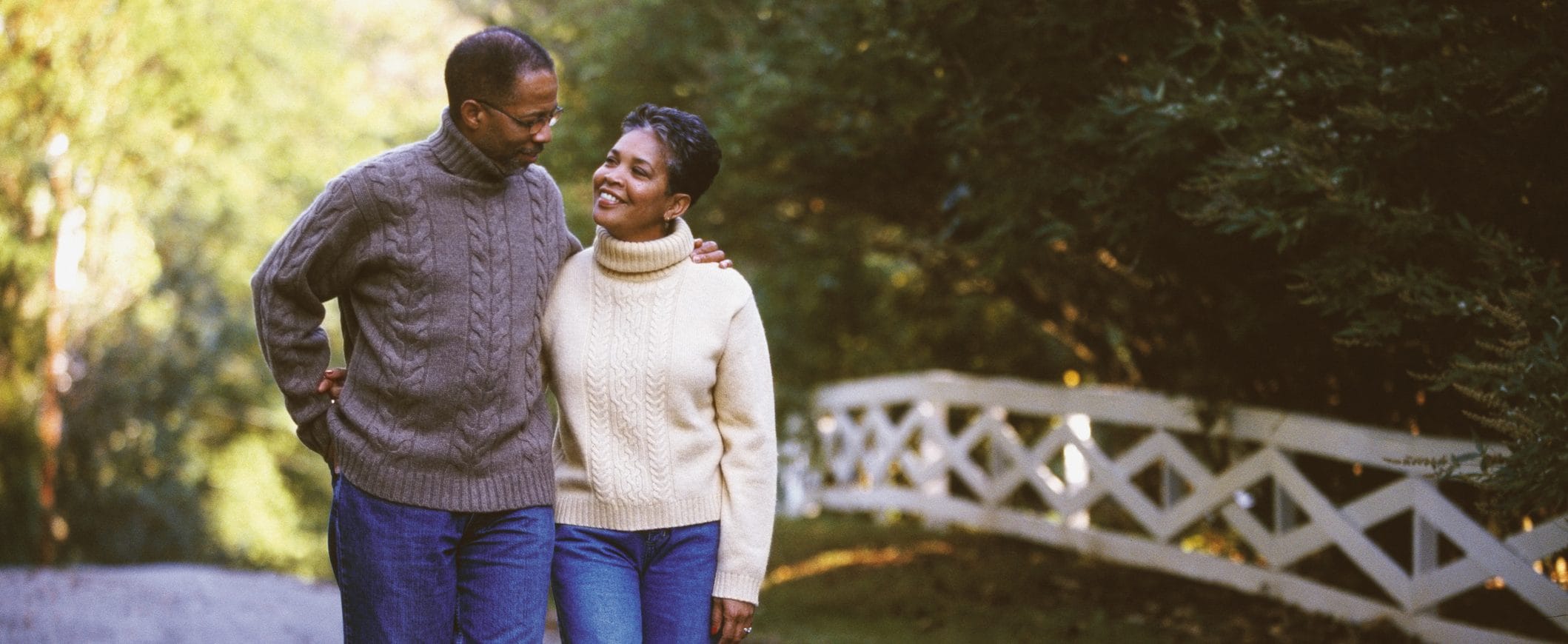 A couple walks outdoors, the man putting his arm on the woman's shoulder.