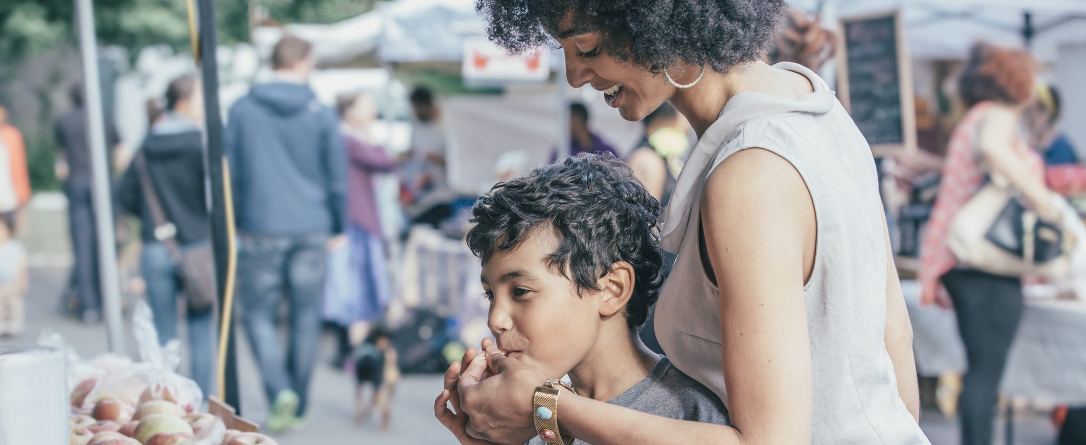 A mother hands her young son a free sample at a farmer’s market.