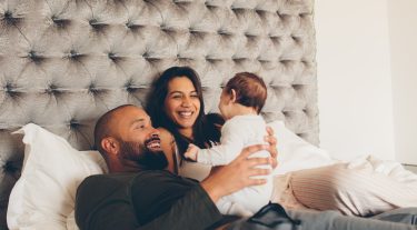 A couple holds their baby in bed.