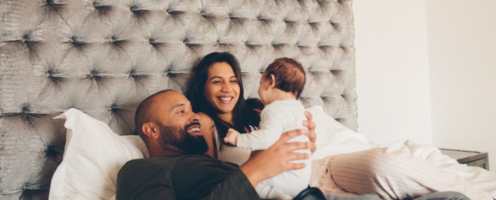 A couple holds their baby in bed.