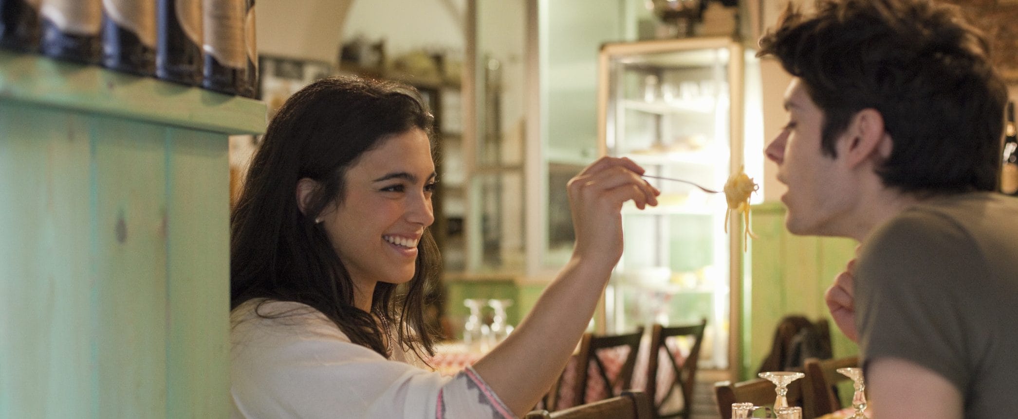 Person happily feeds a fork full of spaghetti to someone else in a restaurant