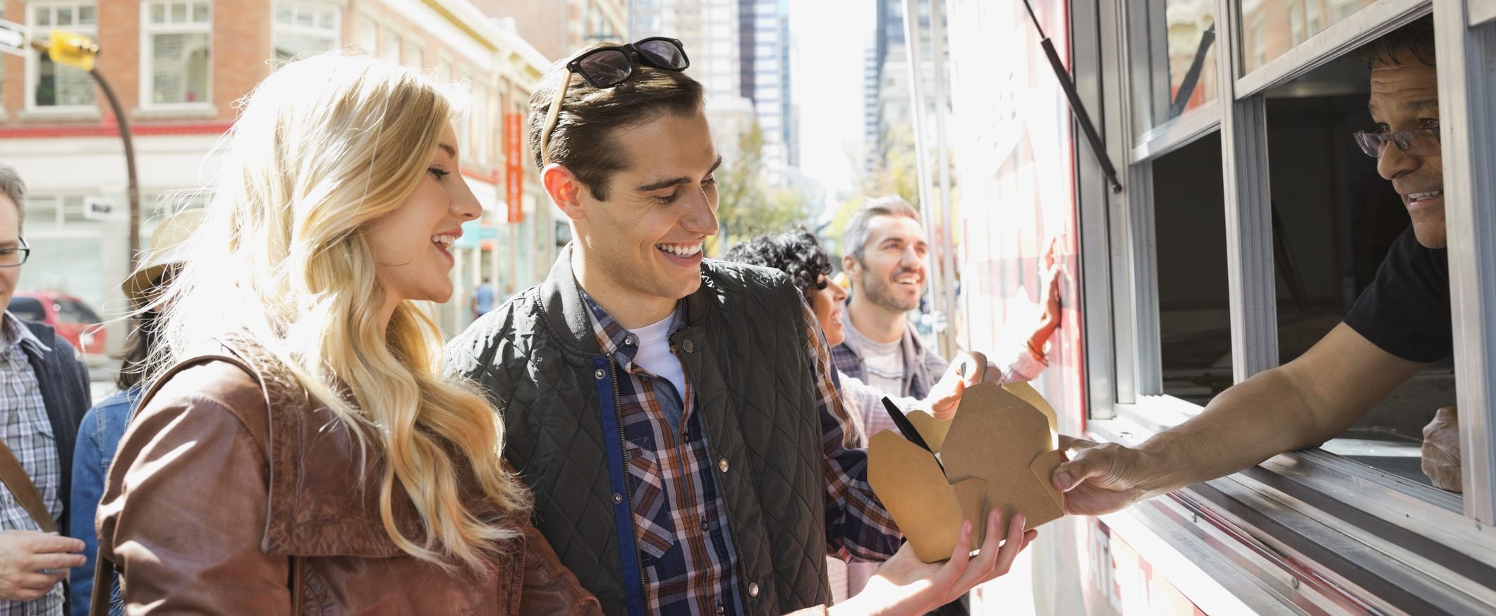 A person in a food truck gives two customers their order as they smile in return