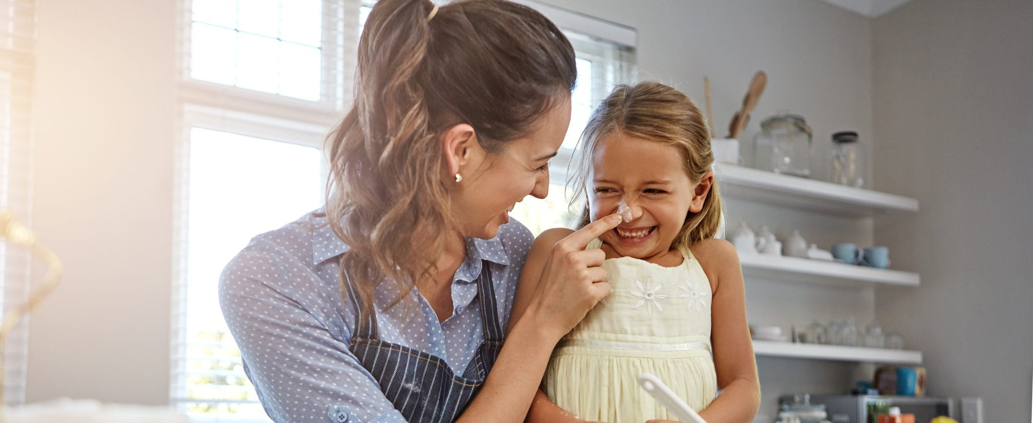 Woman playfully puts flour on a child’s nose as they bake together