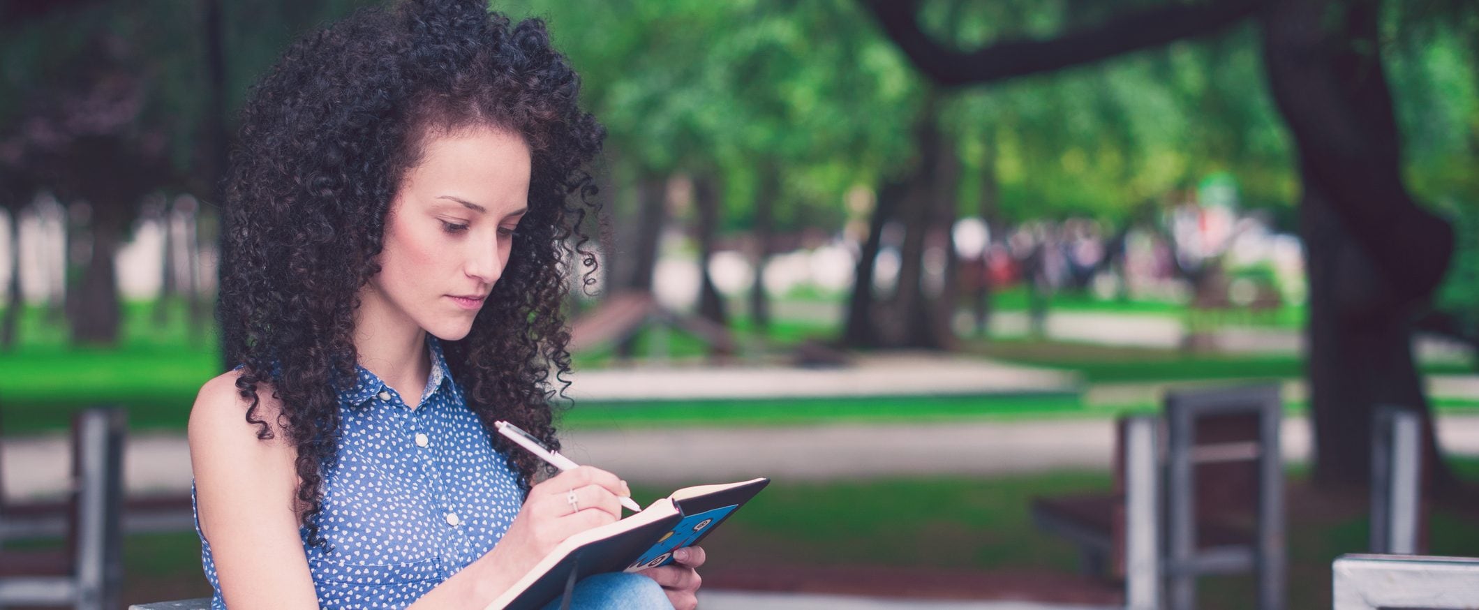 Woman writes in a notebook while sitting in a park