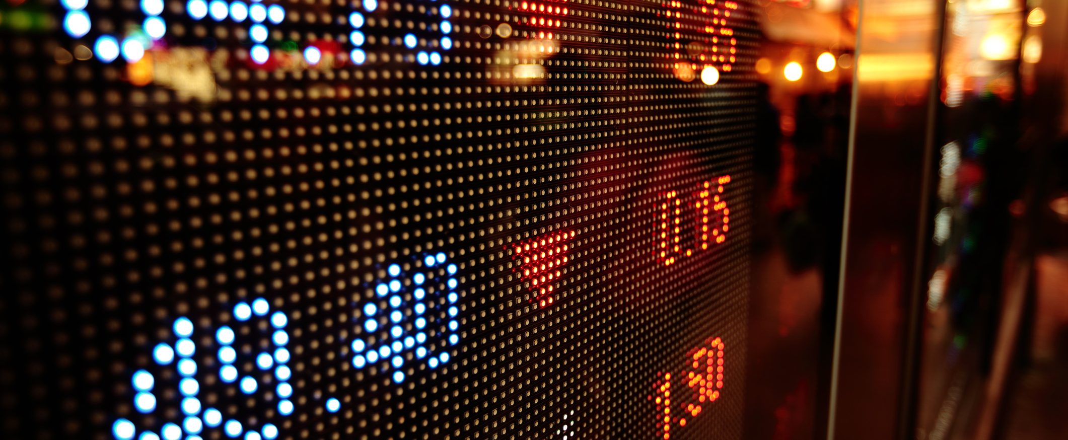 An image of a stock market ticker board with neon numbers and a downward-pointing triangle.