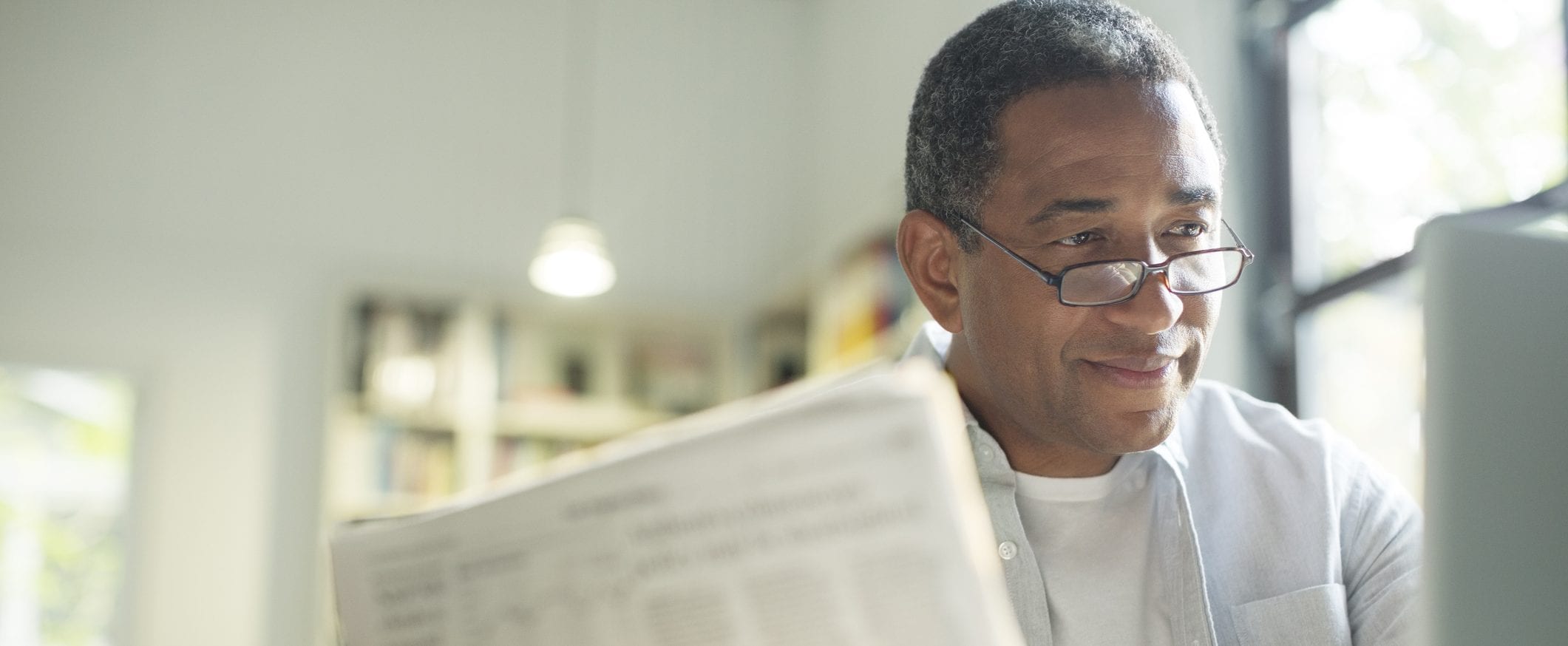 An elderly man wearing glasses with a newspaper in front of him.