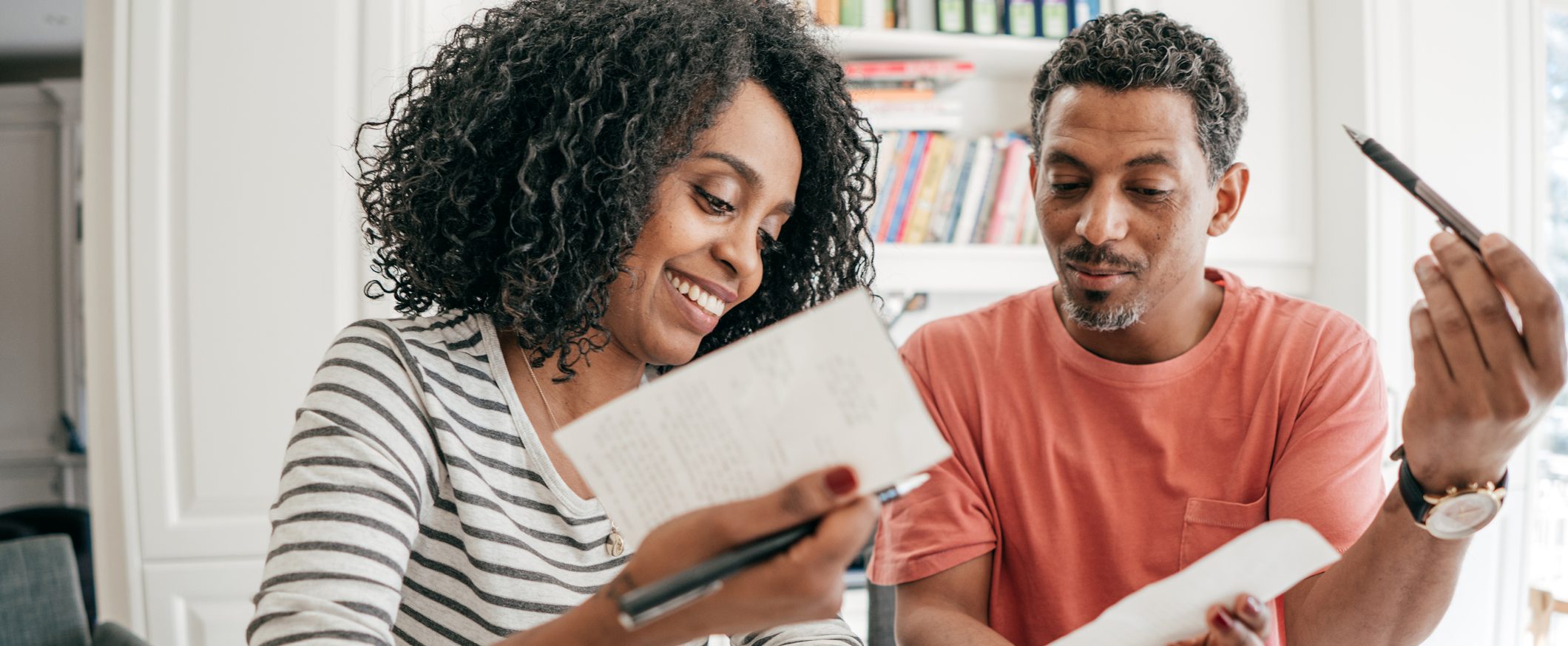 A couple smiling as they look at two receipts, each holding a pen in one of their hands