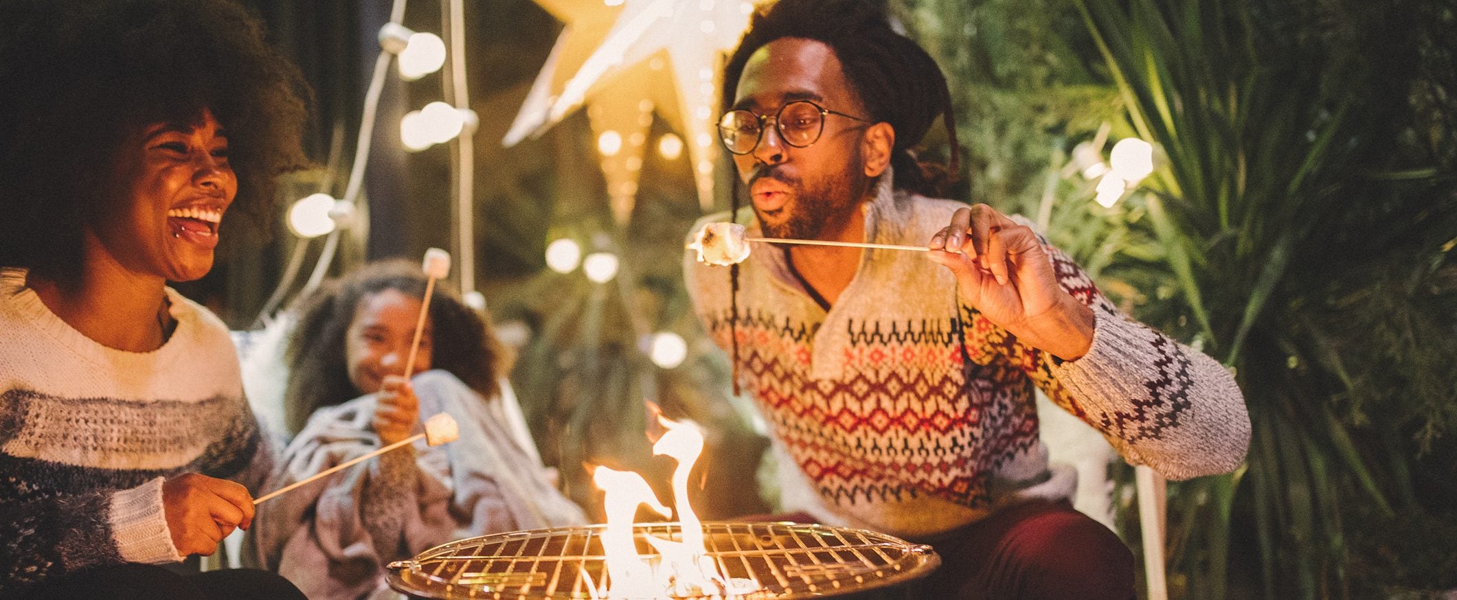 A man, a woman, and a child sit around a fire pit roasting marshmallows.