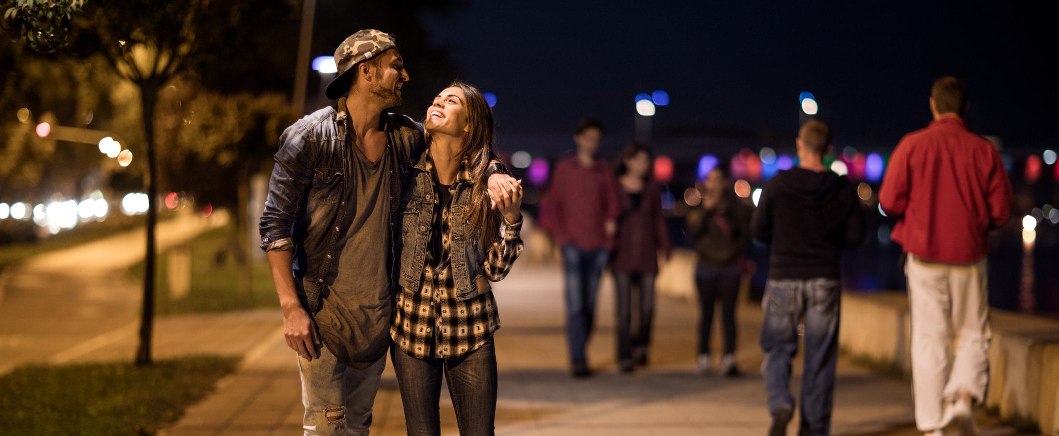 A couple smiles at each other while walking together on a busy sidewalk at night.