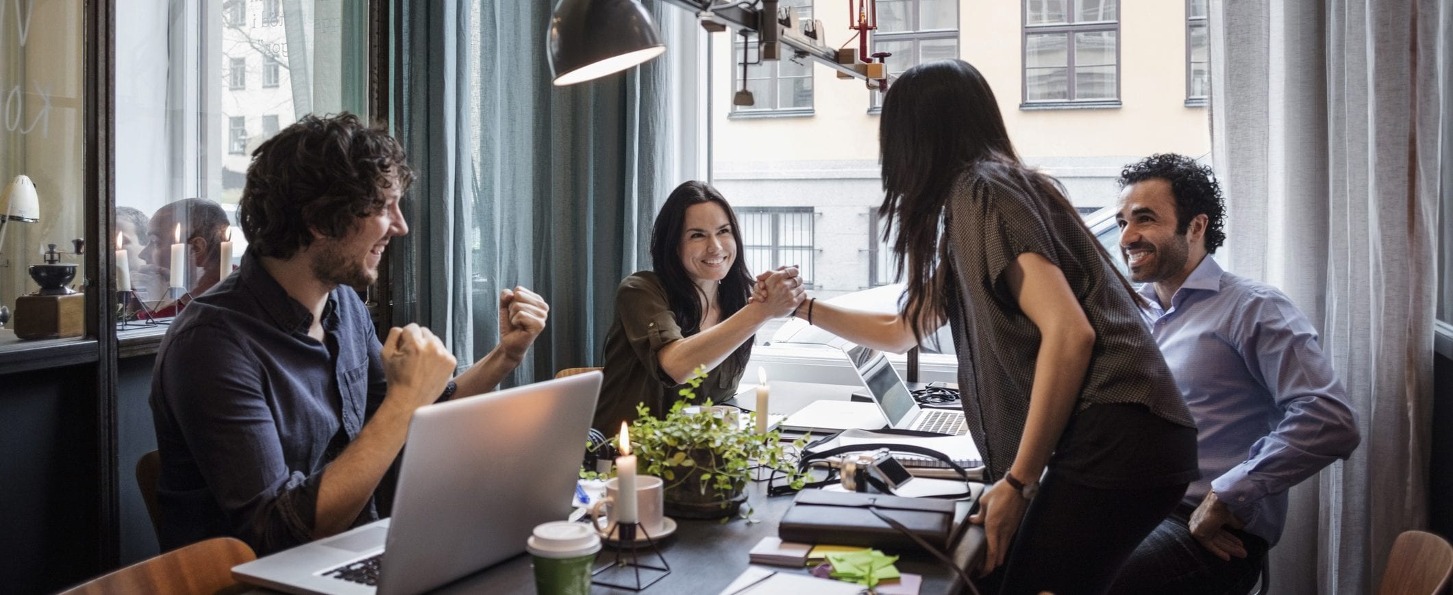 Four people sit at a table. Two of them shake hands.