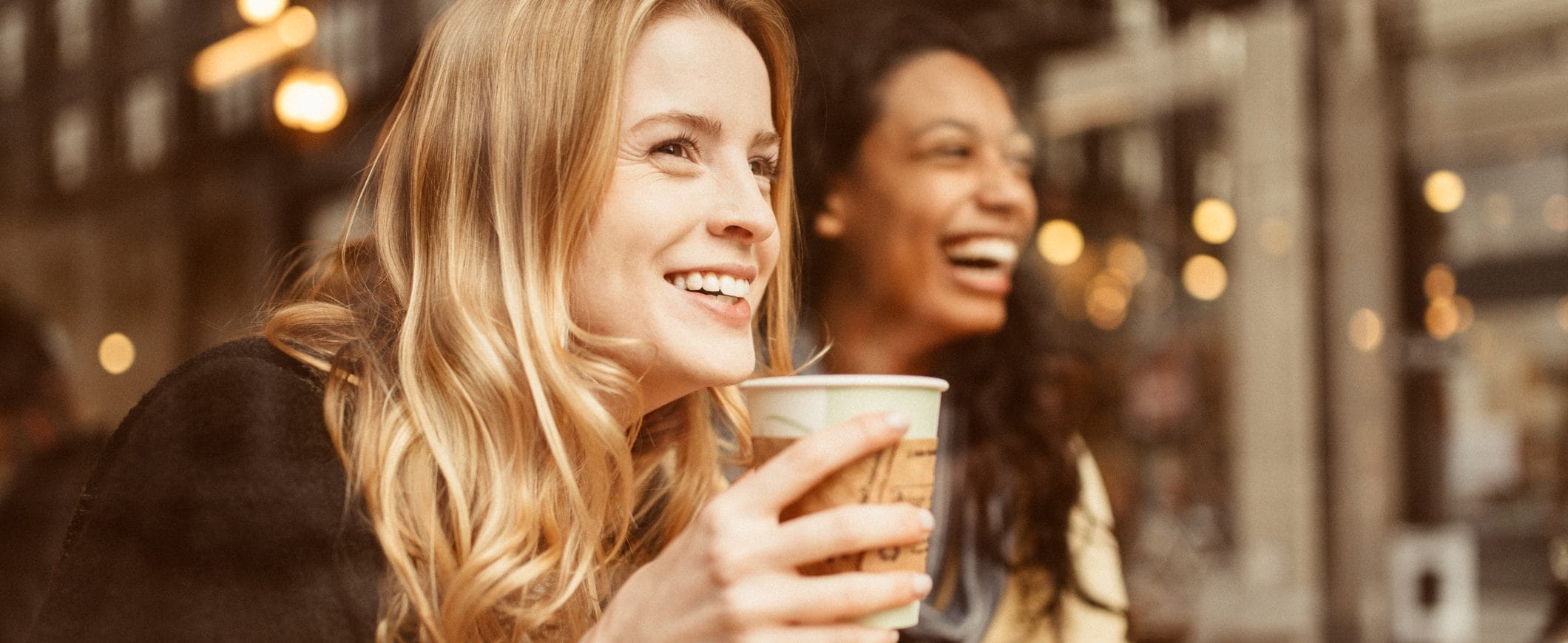 Two women smile, one of them holding a cup of coffee.