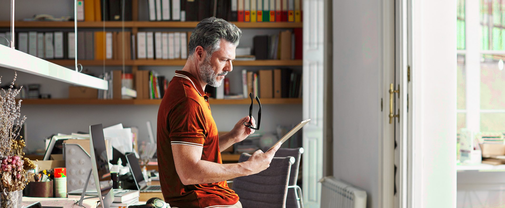 A man holds his glasses while reading a tablet.