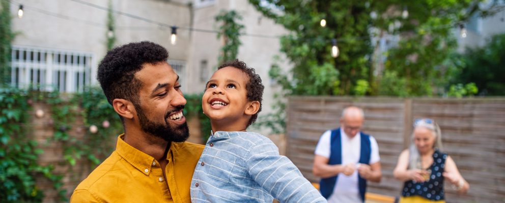 A father holds his son and smiles as they look up to the sky