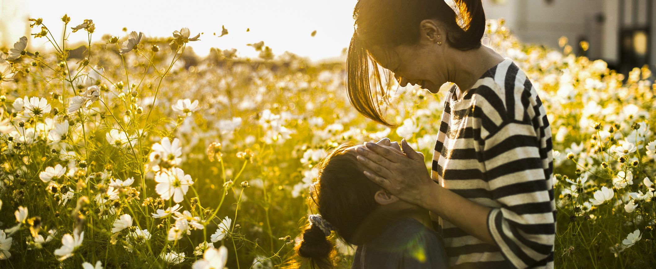 A woman smiles at her young daughter in a field.