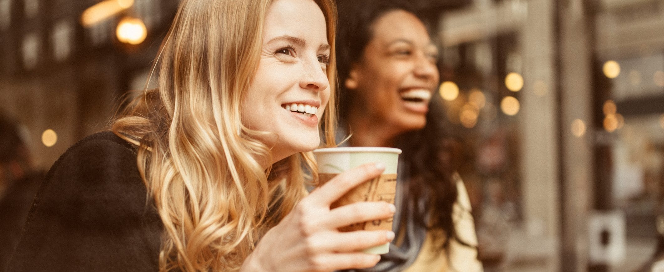 Two women at a coffee shop are laughing.