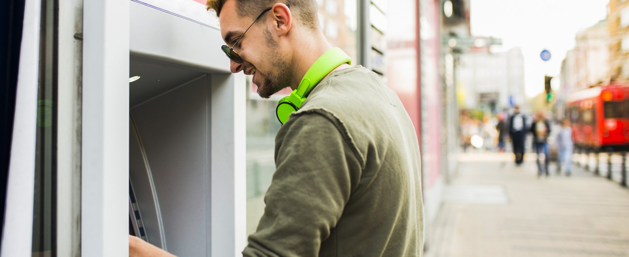 A man standing at an ATM withdraws cash.