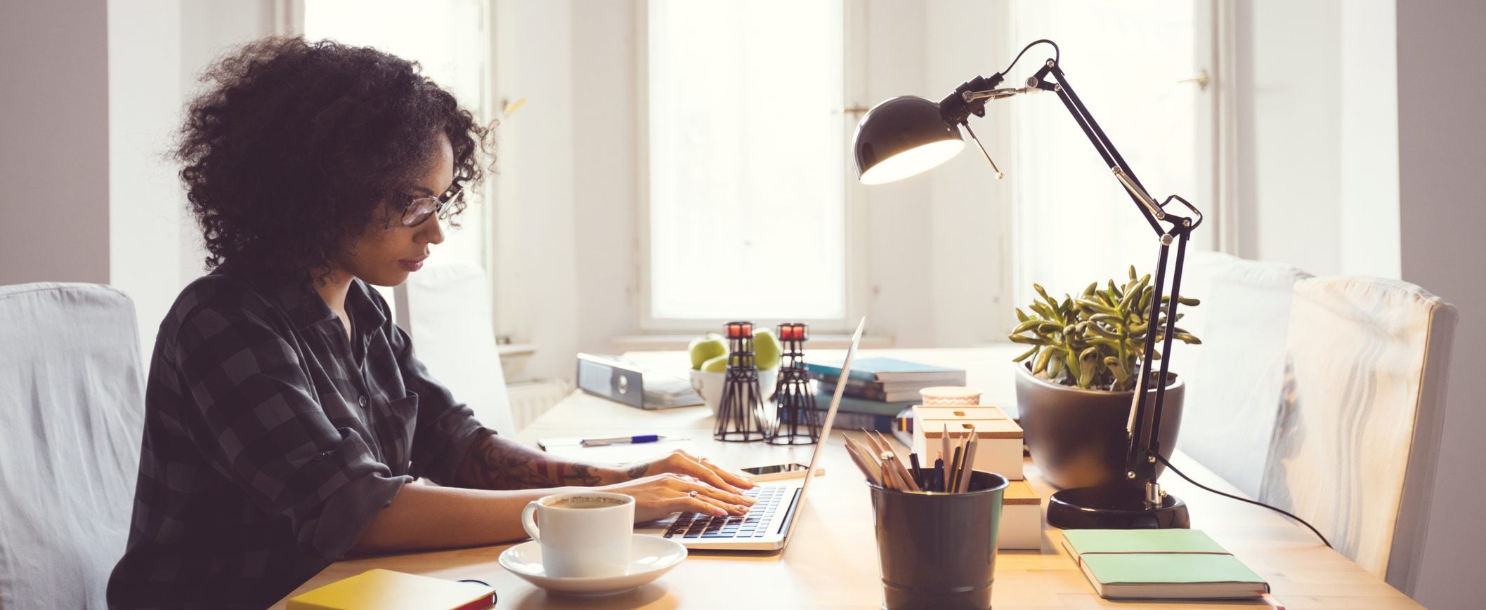 A woman sits at a desk in her home office, working on a laptop.