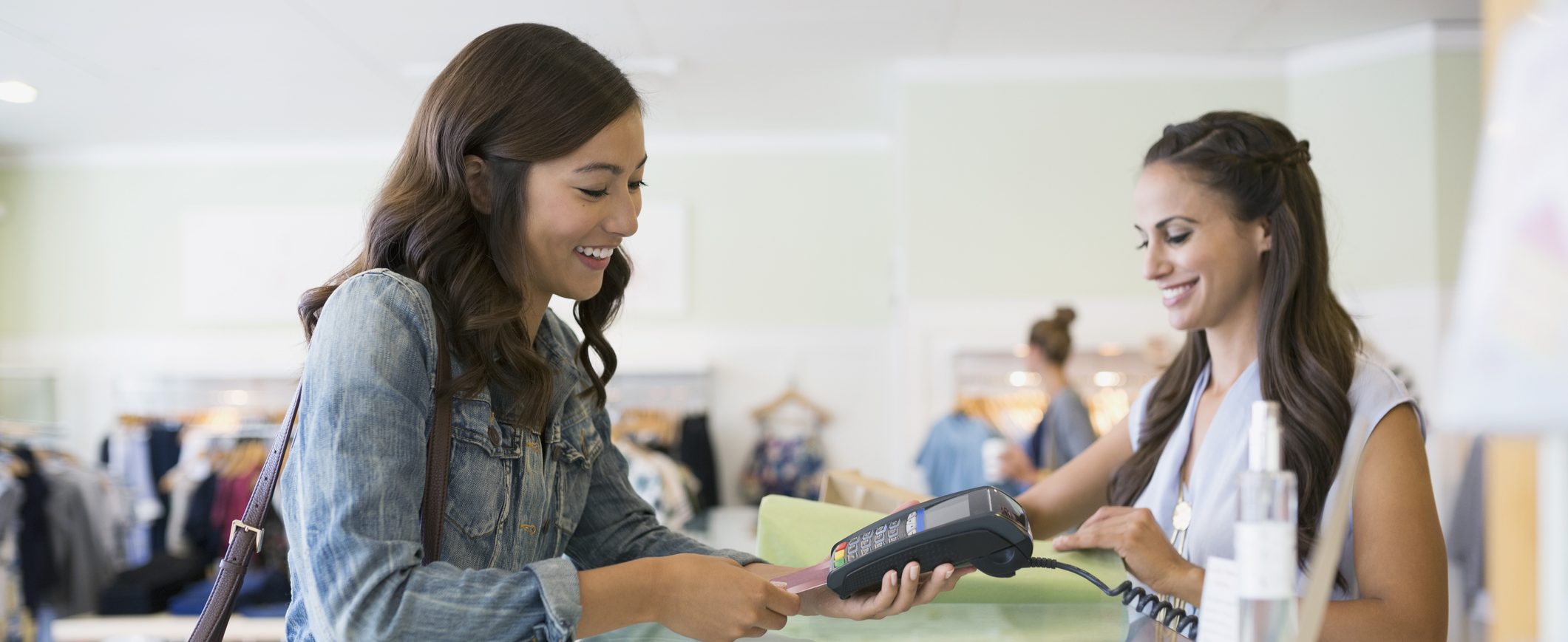 A woman paying with a credit card at store checkout, while the cashier looks on smiling.