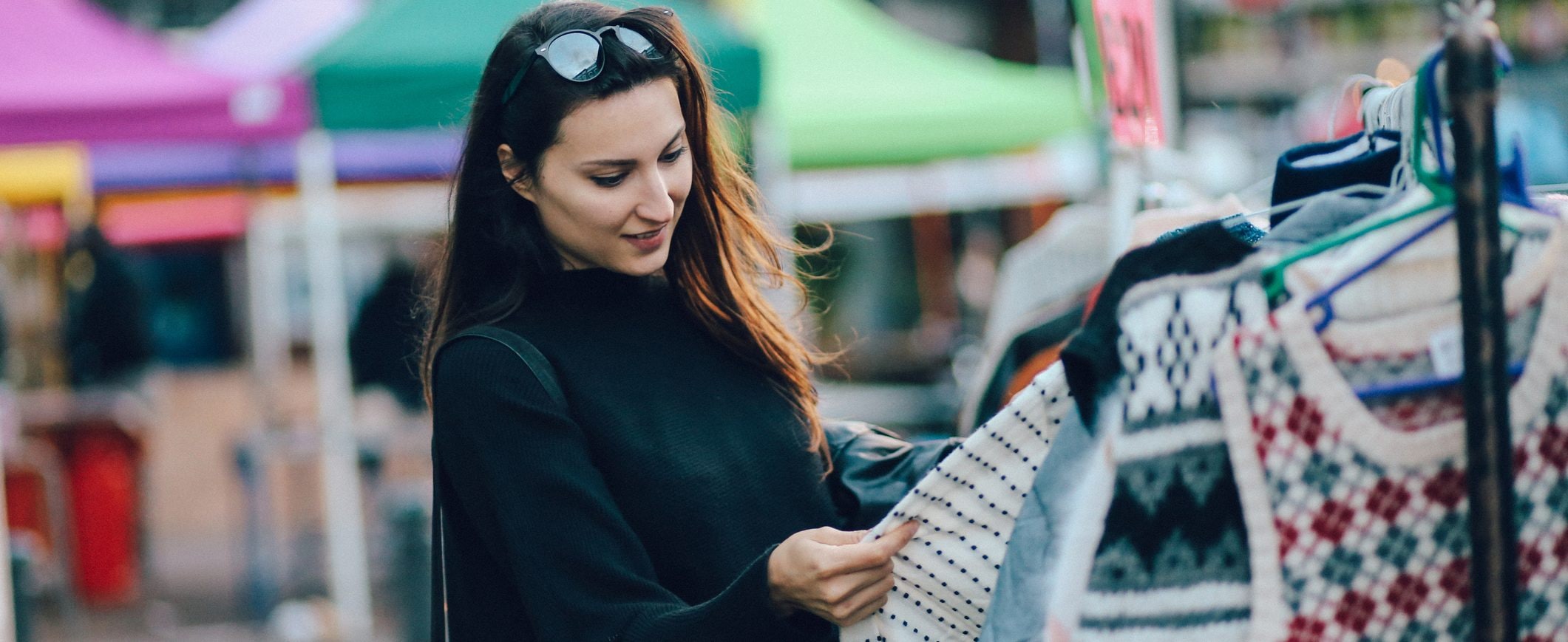 A woman looks at a garment on a rack at a retail store.