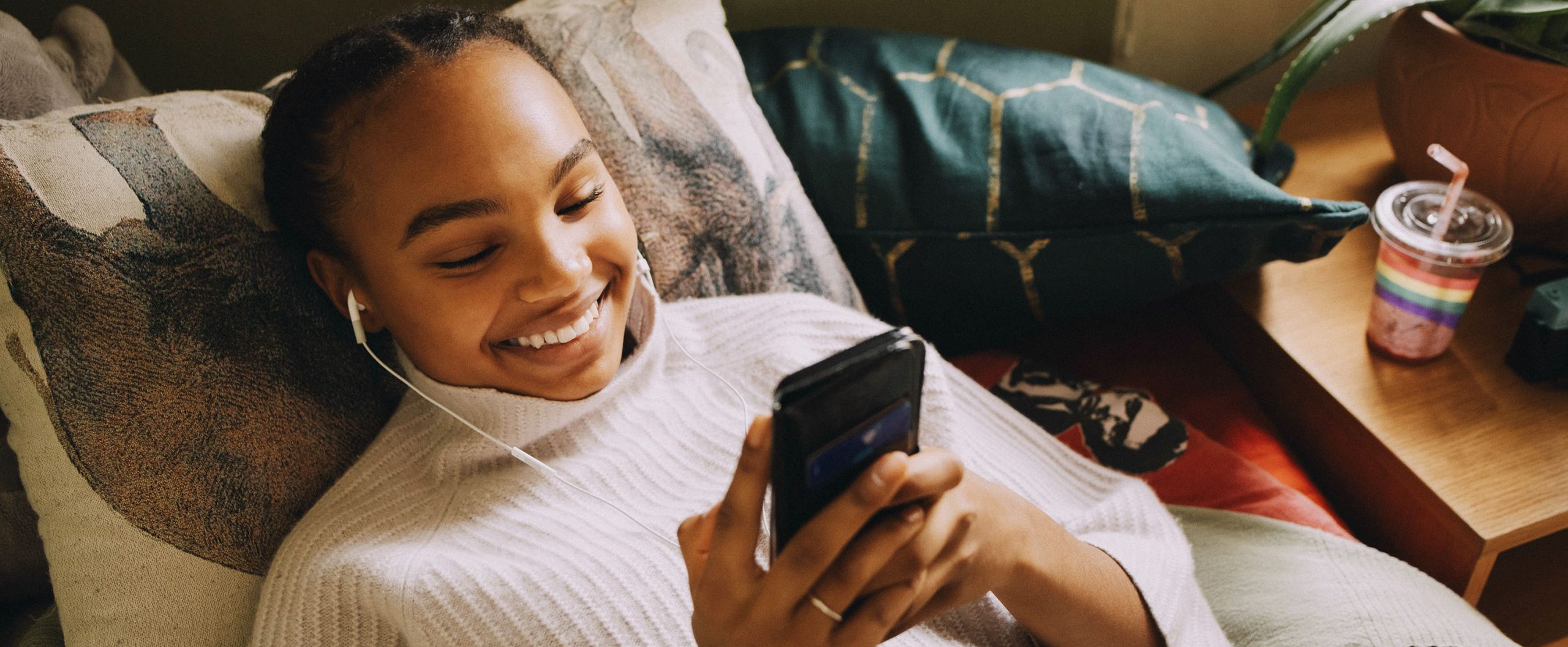 A woman reclines on a pillow and smiles while looking at her mobile phone.