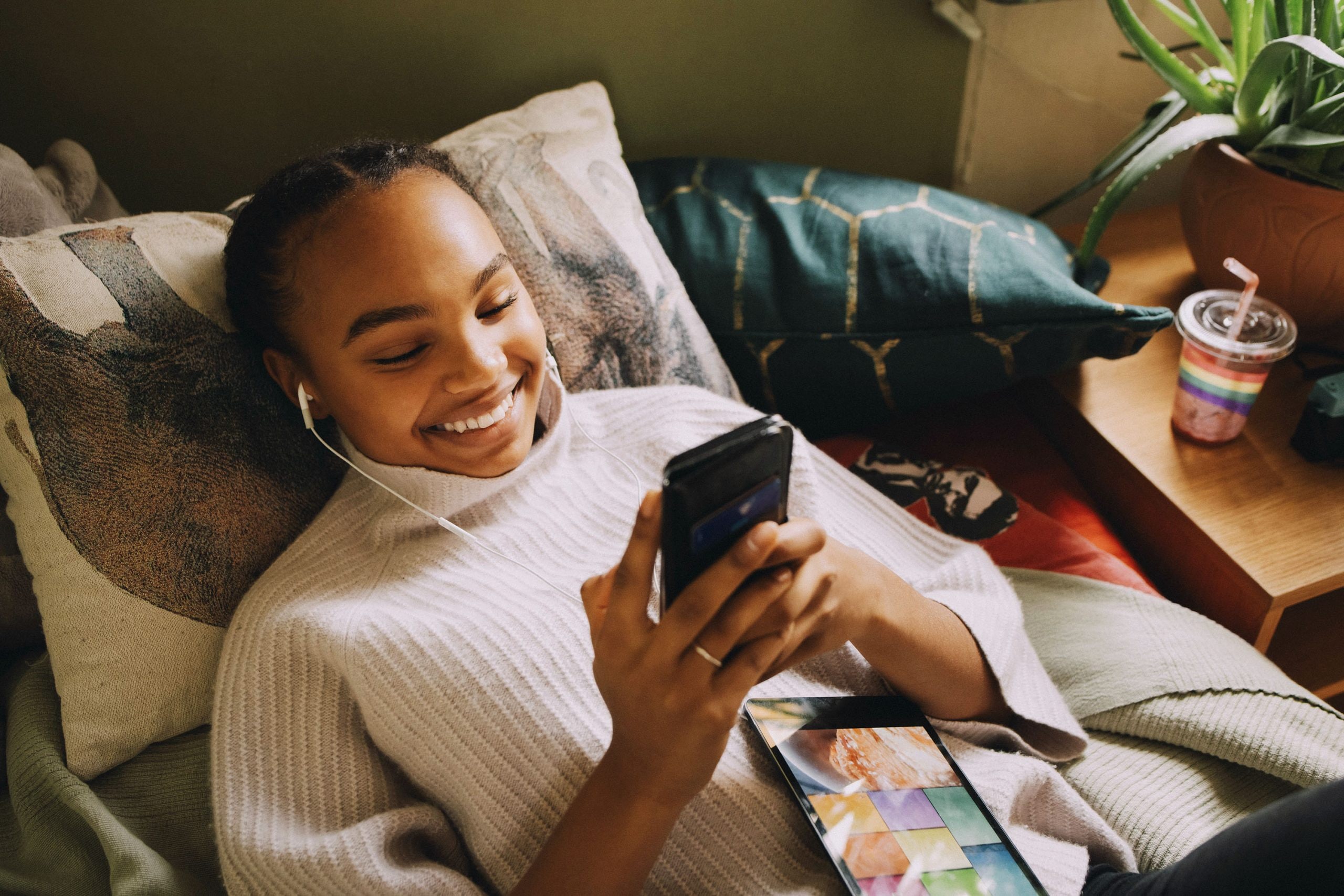 A woman reclines on a pillow and smiles while looking at her mobile phone.