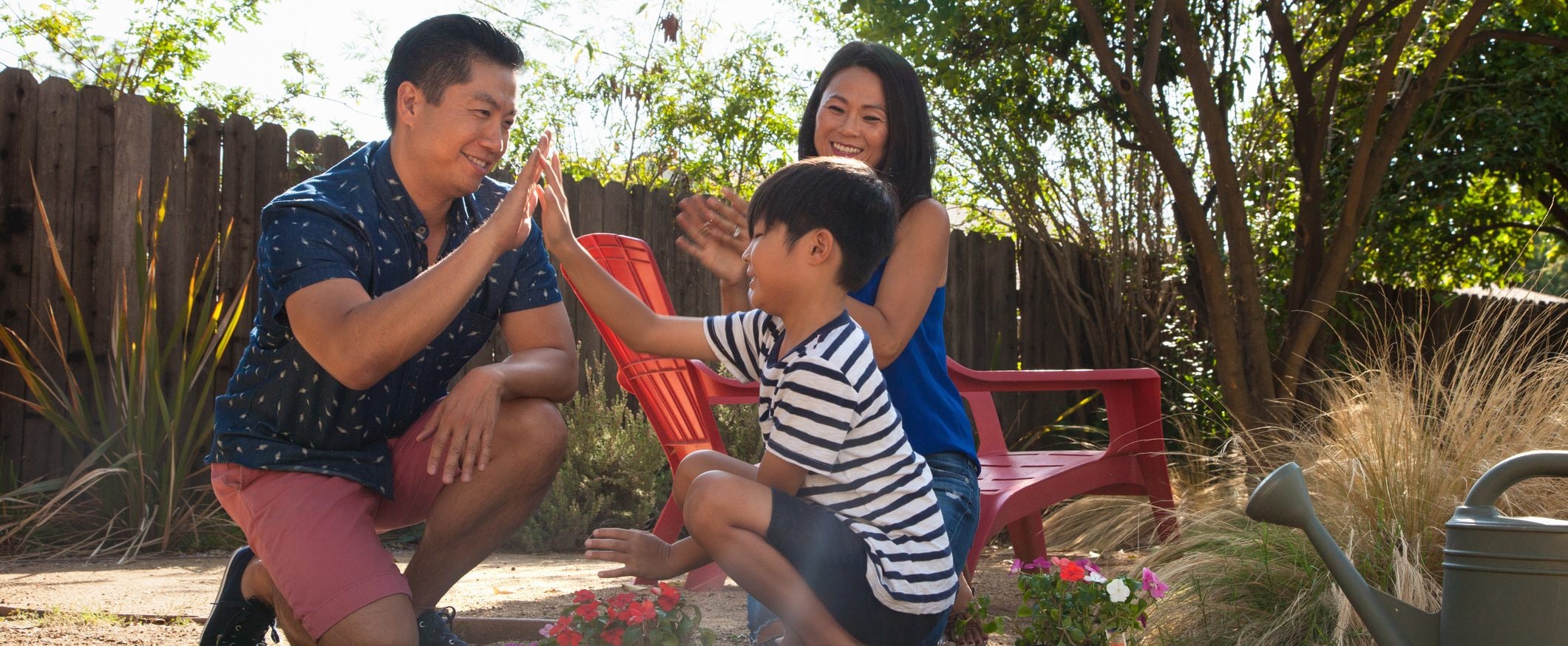 A dad high-fives his son in the backyard as a mom looks on.