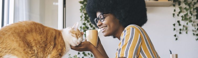 A woman scratches her cat's chin while holding a coffee mug.