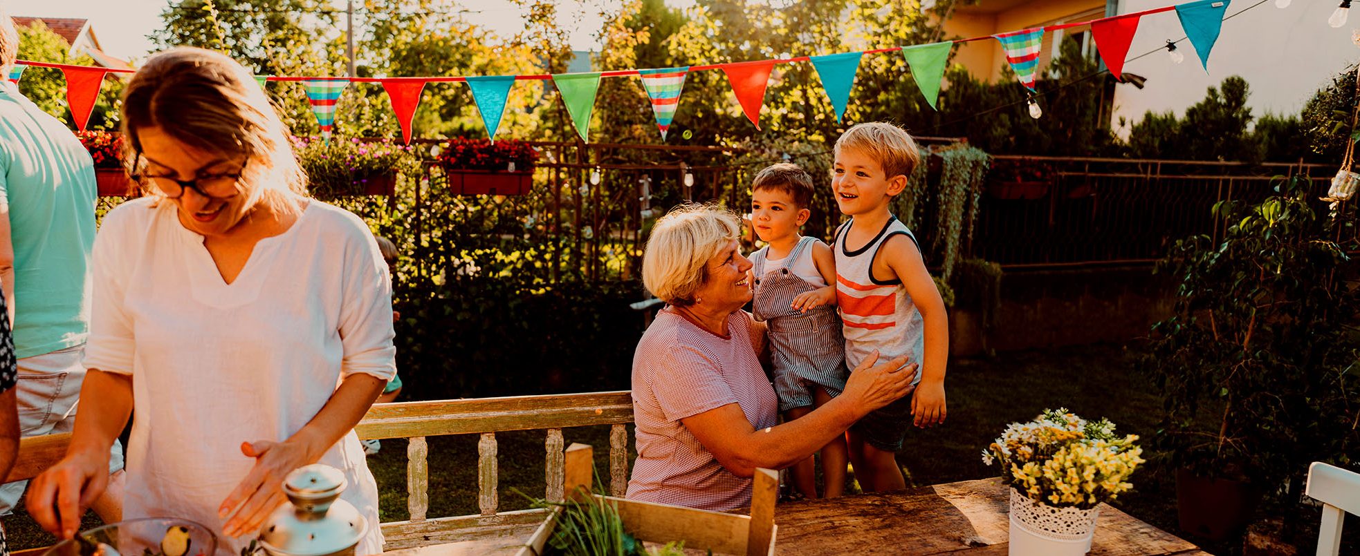 A woman smiles and embraces two young children at a backyard gathering.
