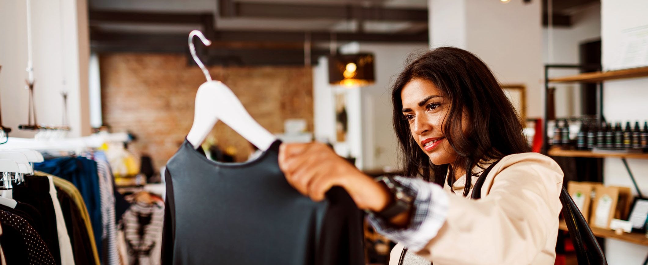 A woman in a boutique considers purchasing a blouse.