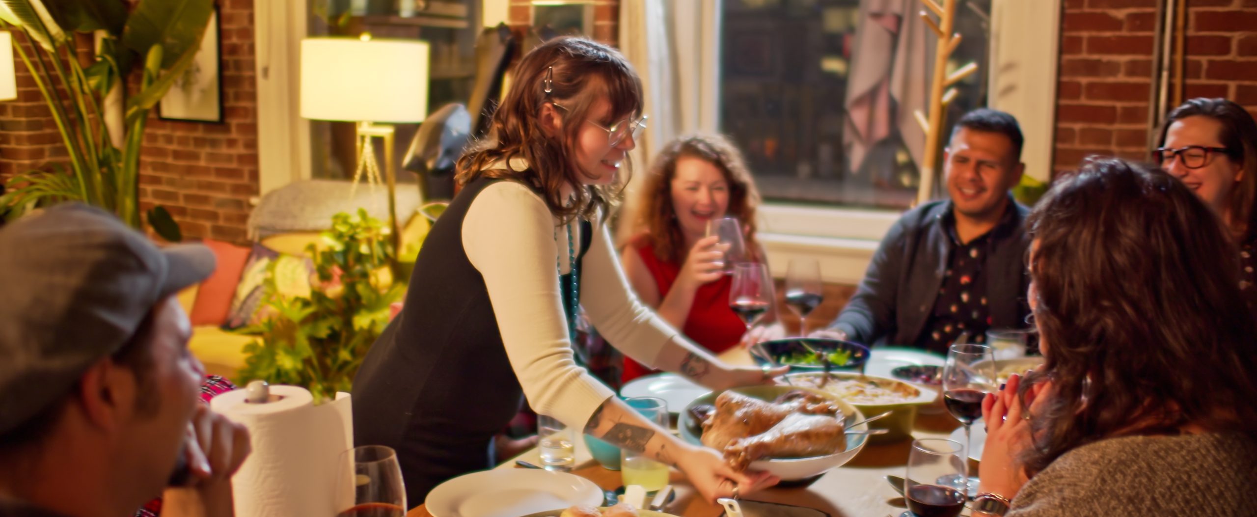 A woman serves a platter to a group gathered around a dining table.