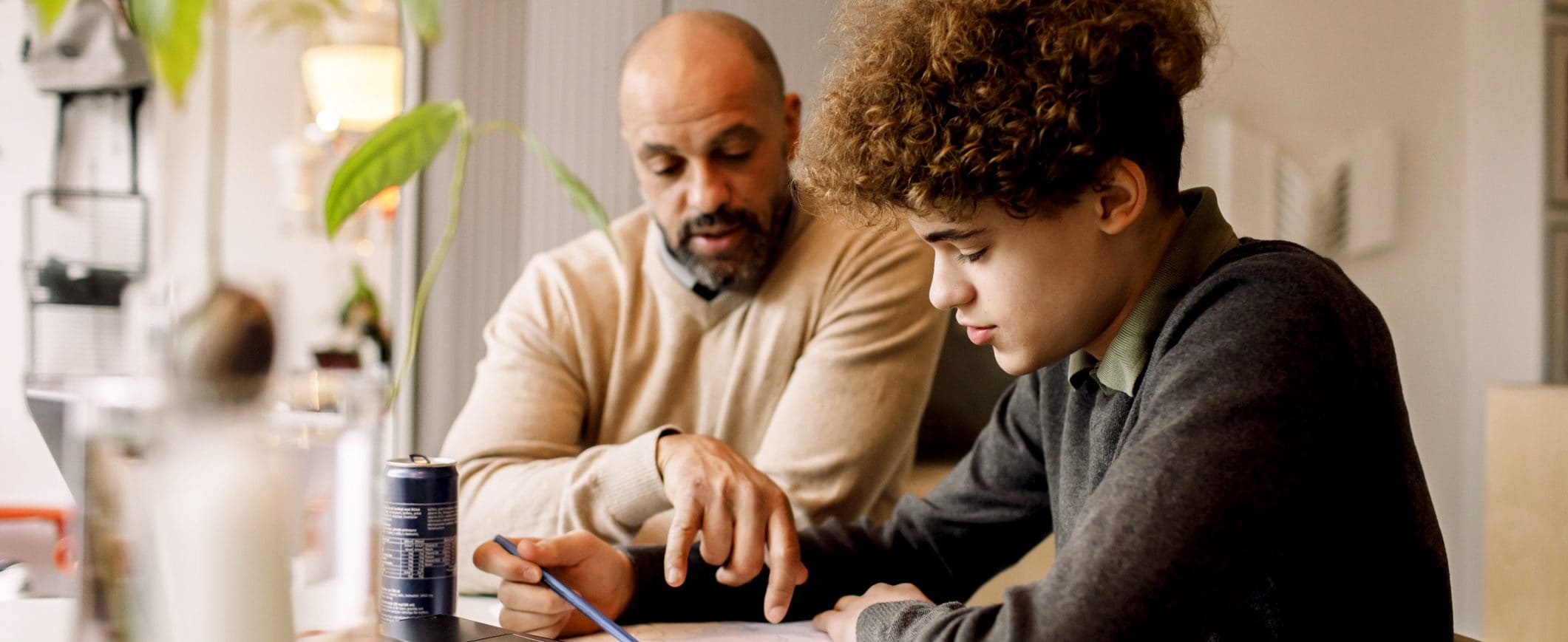 Sitting at a table, a father helps his young son with homework.