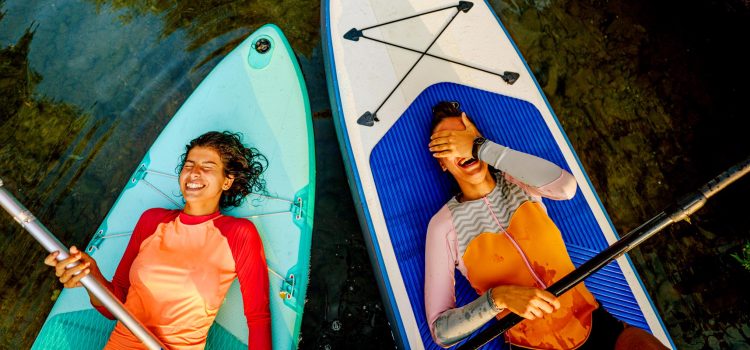 2 women on lie on paddle boards looking up and laughning
