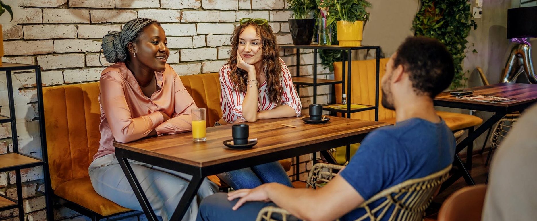 Three friends sit at a café table and talk over cups of coffee and orange juice.