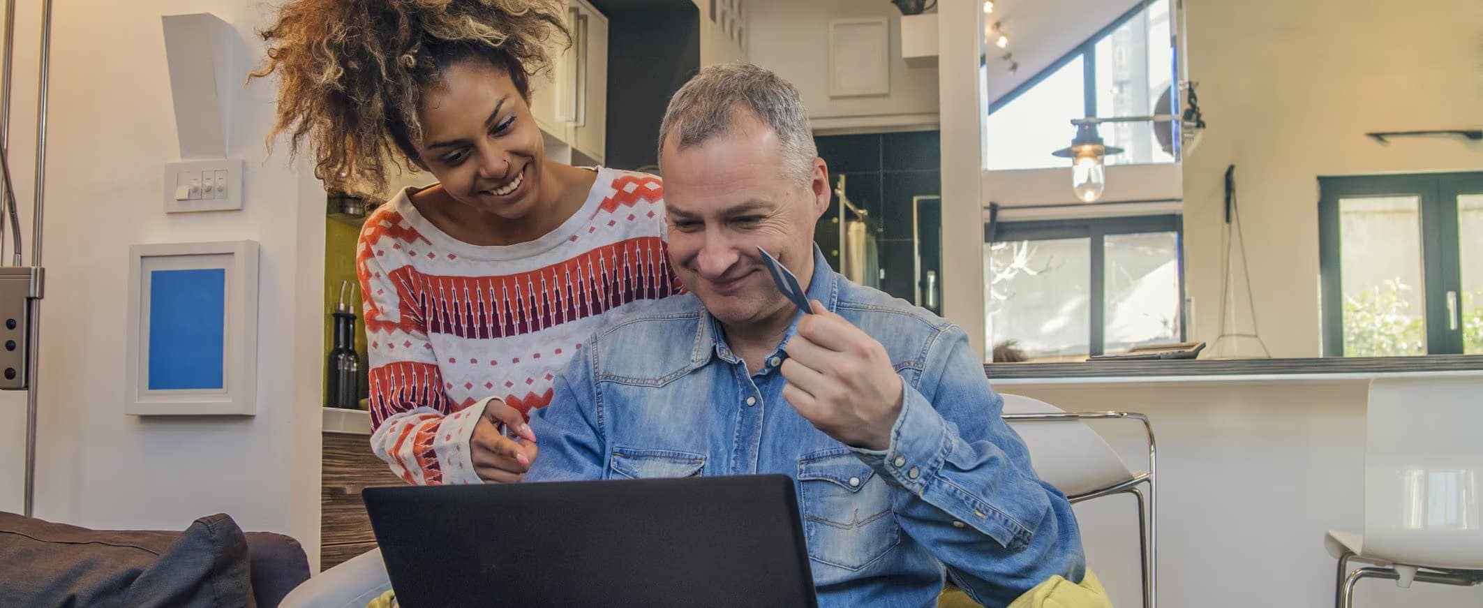A man and a woman, looking at something on a laptop computer together in their living room.